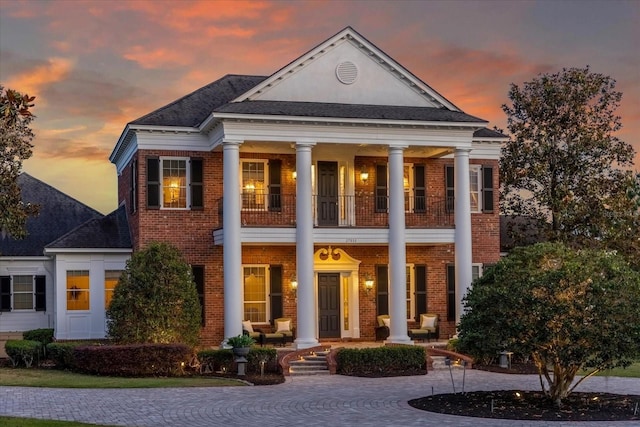 greek revival inspired property with a porch, brick siding, and a balcony