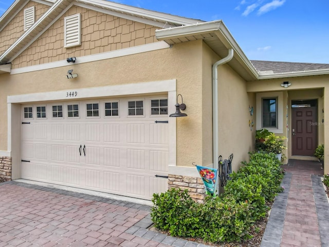 view of front of property with a garage, stone siding, decorative driveway, and stucco siding