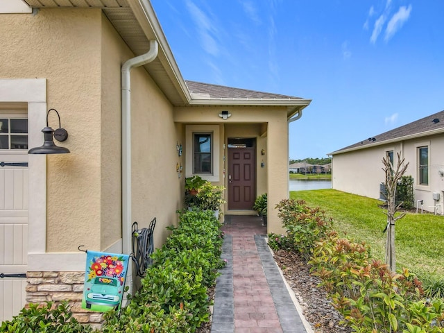 doorway to property featuring a water view, a yard, and stucco siding