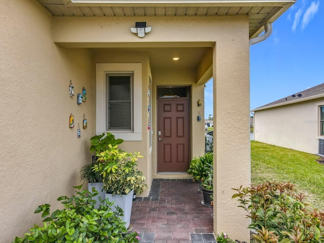 view of exterior entry featuring a lawn and stucco siding