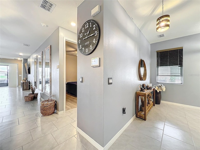 corridor featuring visible vents, baseboards, and light tile patterned floors