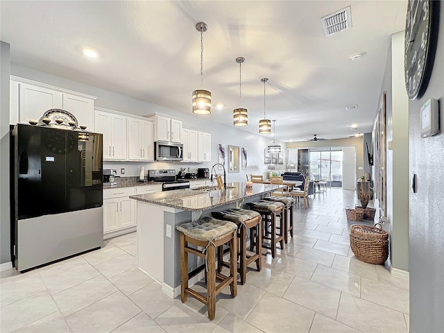 kitchen with a breakfast bar area, stainless steel appliances, a sink, visible vents, and dark stone counters