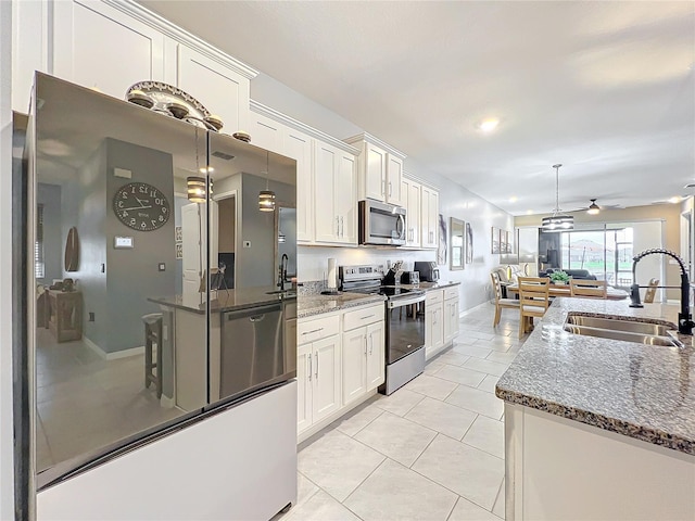 kitchen featuring appliances with stainless steel finishes, open floor plan, white cabinets, a sink, and light tile patterned flooring