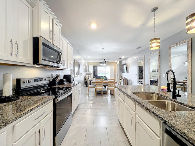 kitchen with light tile patterned flooring, stainless steel appliances, a sink, open floor plan, and hanging light fixtures