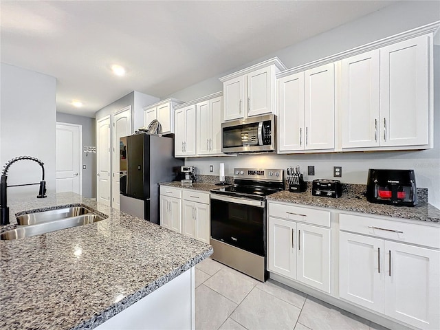 kitchen with stainless steel appliances, light tile patterned flooring, a sink, and white cabinetry