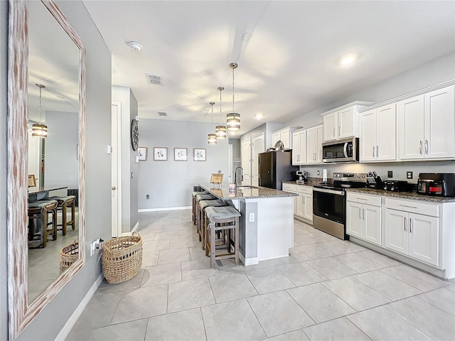 kitchen featuring a sink, white cabinetry, appliances with stainless steel finishes, a kitchen bar, and a center island with sink