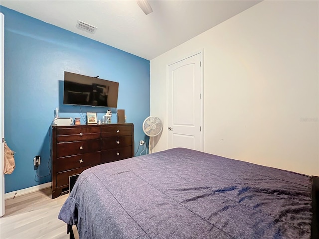 bedroom with a ceiling fan, visible vents, baseboards, and wood finished floors