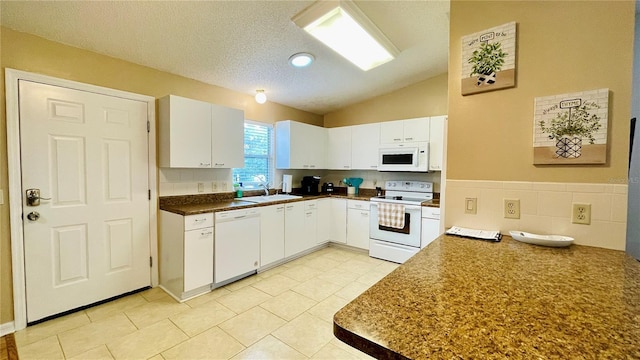 kitchen featuring dark countertops, white cabinetry, vaulted ceiling, a sink, and white appliances