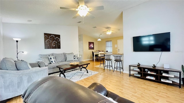 living room with light wood-style floors, a ceiling fan, vaulted ceiling, a textured ceiling, and baseboards