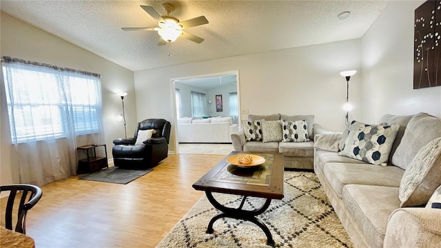 living area with lofted ceiling, light wood-type flooring, a ceiling fan, and a textured ceiling