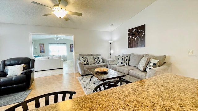 living room featuring lofted ceiling, light wood finished floors, a textured ceiling, and a ceiling fan