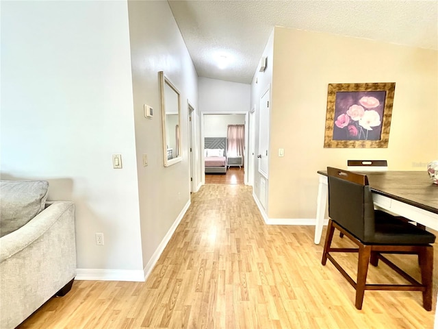 corridor with a textured ceiling, vaulted ceiling, light wood-type flooring, and baseboards