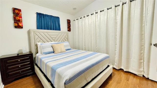 bedroom featuring a textured ceiling, vaulted ceiling, and wood finished floors