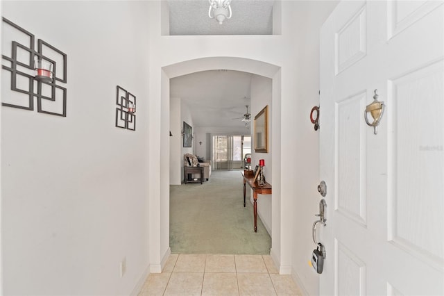 hallway with light tile patterned floors, baseboards, arched walkways, and light colored carpet