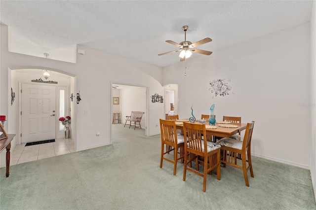 dining room featuring arched walkways, a textured ceiling, light carpet, and a ceiling fan