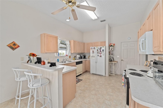 kitchen featuring a breakfast bar, light brown cabinets, a sink, white appliances, and a peninsula