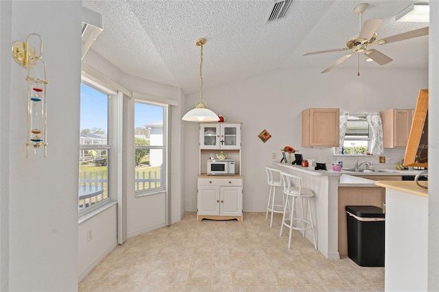 kitchen with lofted ceiling, white microwave, visible vents, light countertops, and a kitchen bar