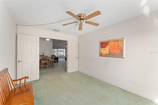 carpeted spare room with baseboards, ceiling fan, visible vents, and a textured ceiling