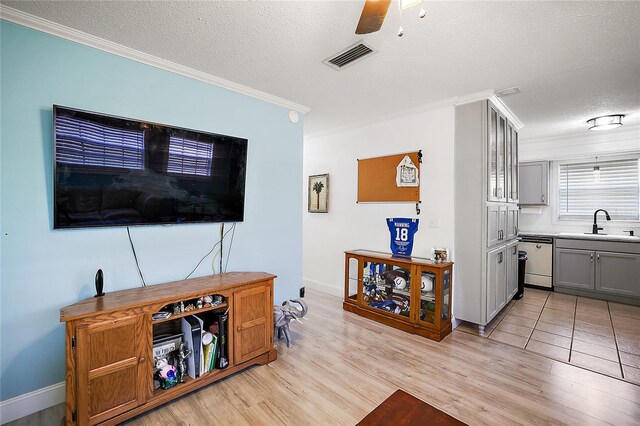 living area featuring a textured ceiling, ceiling fan, visible vents, ornamental molding, and light wood-type flooring