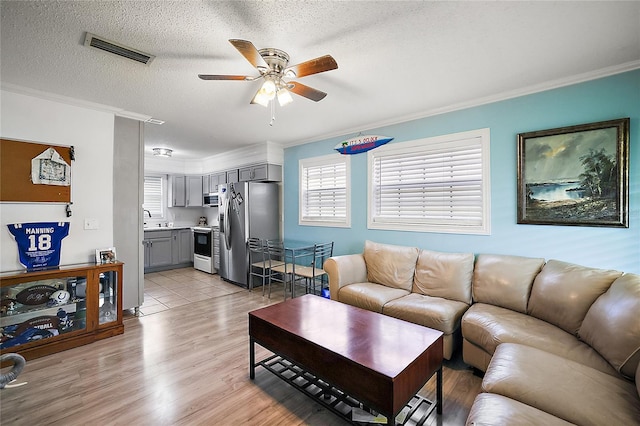 living area featuring ornamental molding, visible vents, a textured ceiling, and light wood finished floors