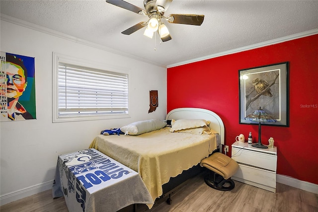 bedroom with baseboards, an accent wall, wood finished floors, crown molding, and a textured ceiling