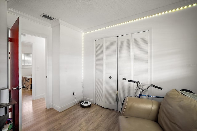 living area with a textured ceiling, light wood-style flooring, visible vents, baseboards, and ornamental molding