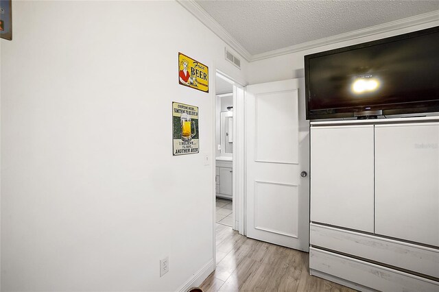 hall featuring a textured ceiling, ornamental molding, wood finished floors, and visible vents