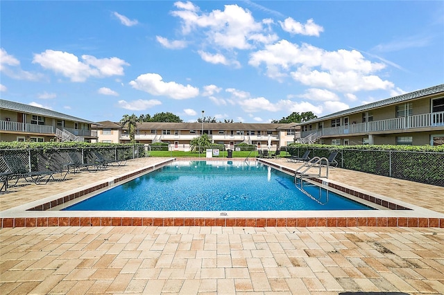 community pool with a patio, fence, and a residential view