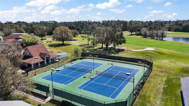 view of sport court featuring golf course view, a water view, fence, and a lawn