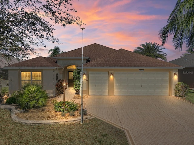 ranch-style home with driveway, roof with shingles, an attached garage, and stucco siding