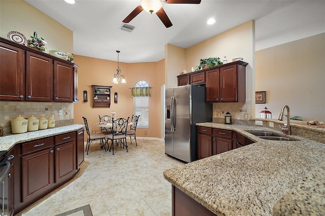 kitchen featuring light stone counters, decorative light fixtures, backsplash, a sink, and stainless steel fridge