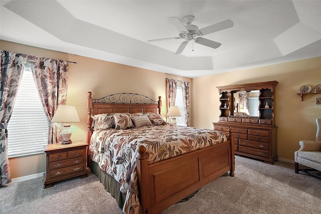 bedroom with a tray ceiling, light carpet, ceiling fan, and baseboards