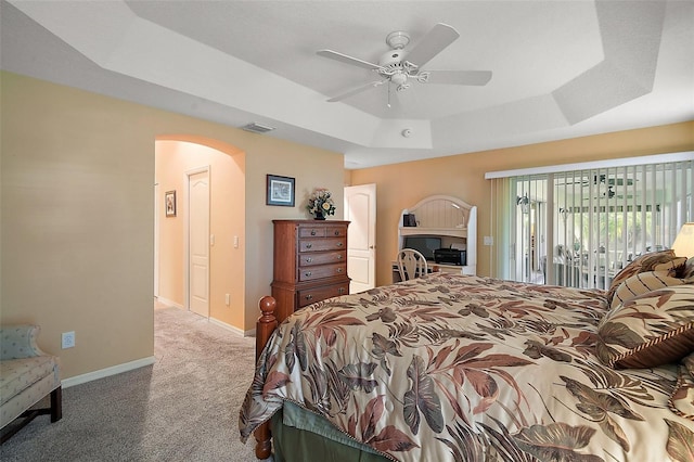 bedroom featuring baseboards, arched walkways, access to exterior, a tray ceiling, and carpet floors