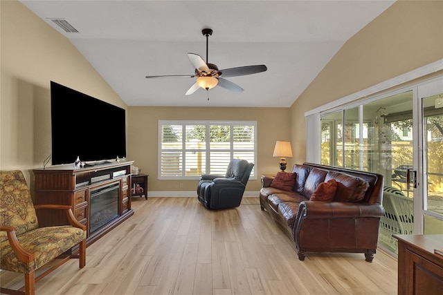 living area featuring visible vents, a ceiling fan, vaulted ceiling, light wood-type flooring, and a glass covered fireplace