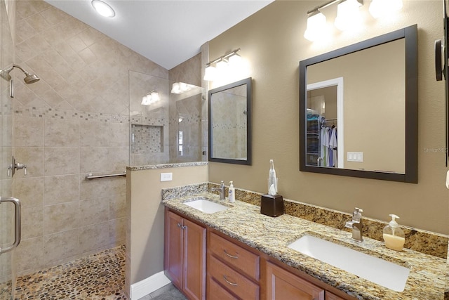 bathroom with double vanity, a tile shower, a sink, and a walk in closet