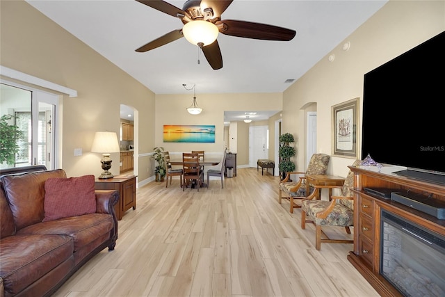 living room featuring visible vents, light wood-style flooring, a ceiling fan, a glass covered fireplace, and baseboards