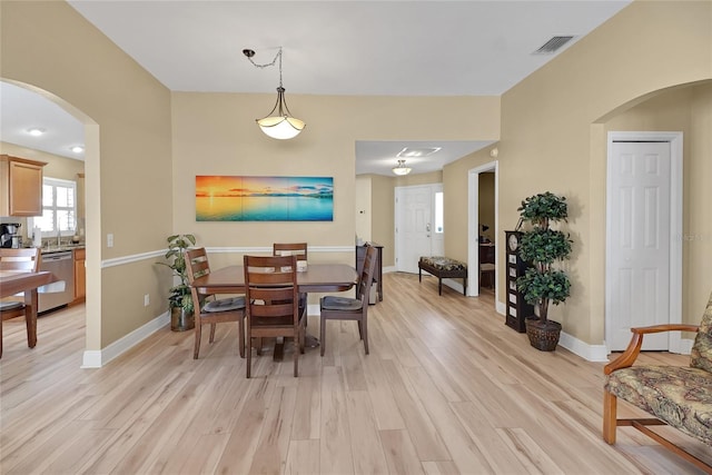 dining room featuring arched walkways, light wood-style flooring, visible vents, and baseboards