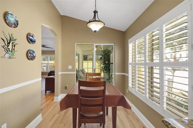 dining area with arched walkways, baseboards, a ceiling fan, vaulted ceiling, and light wood-type flooring