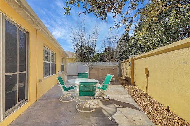 view of patio / terrace with an outbuilding, a storage shed, outdoor dining space, and a fenced backyard