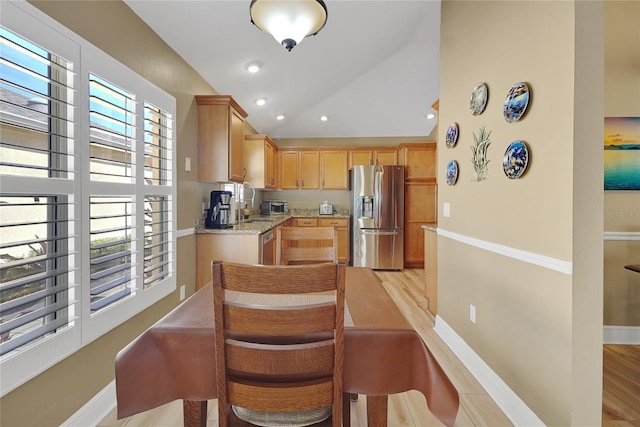 kitchen with baseboards, stainless steel fridge with ice dispenser, light stone countertops, vaulted ceiling, and light wood-style floors