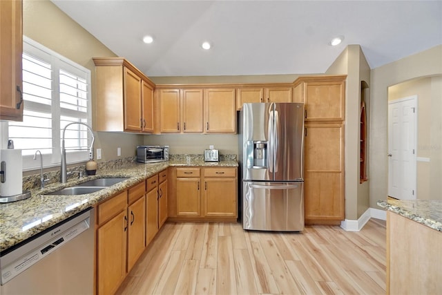 kitchen with vaulted ceiling, appliances with stainless steel finishes, a sink, and light wood-style floors