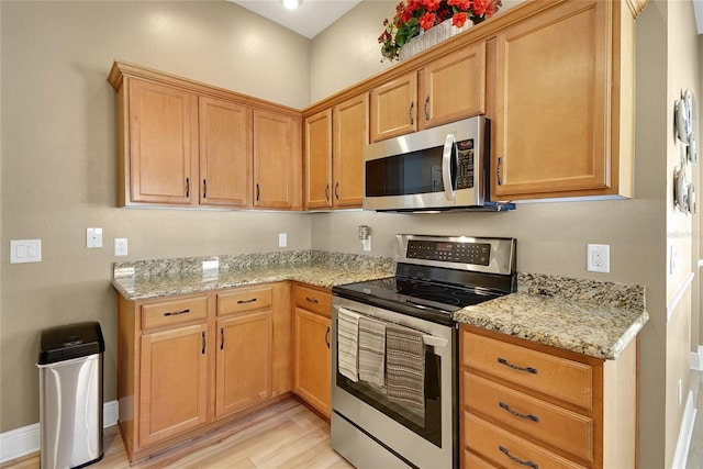 kitchen with light wood finished floors, baseboards, light stone counters, and stainless steel appliances