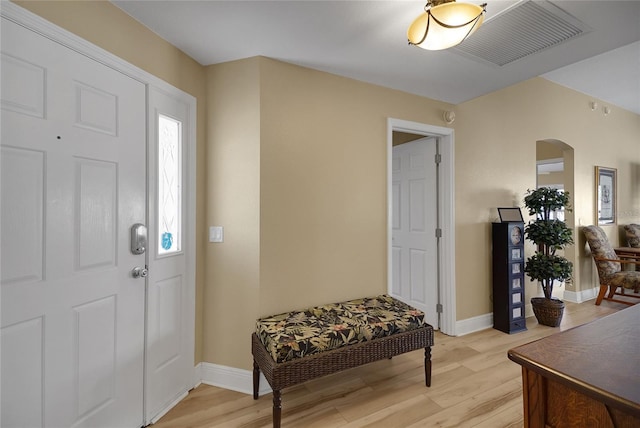 foyer entrance with light wood finished floors, baseboards, visible vents, and arched walkways