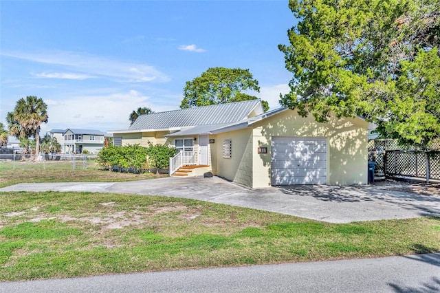 ranch-style home featuring concrete driveway, metal roof, an attached garage, fence, and a front yard