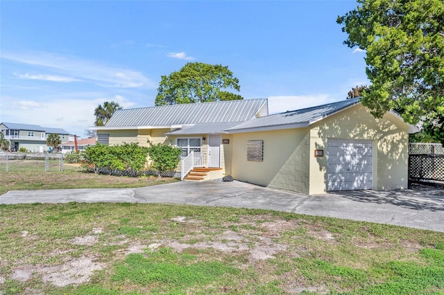 ranch-style house featuring metal roof, an attached garage, concrete block siding, fence, and driveway