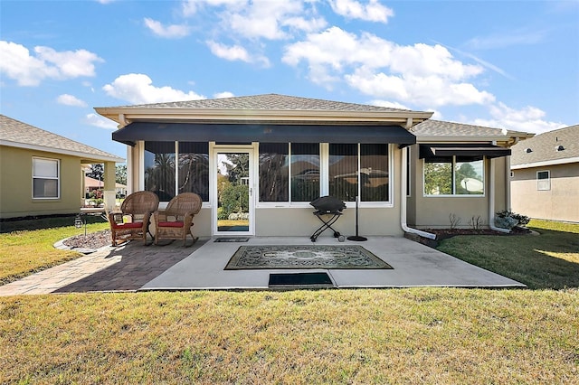 back of property with a shingled roof, a sunroom, a yard, a patio area, and stucco siding