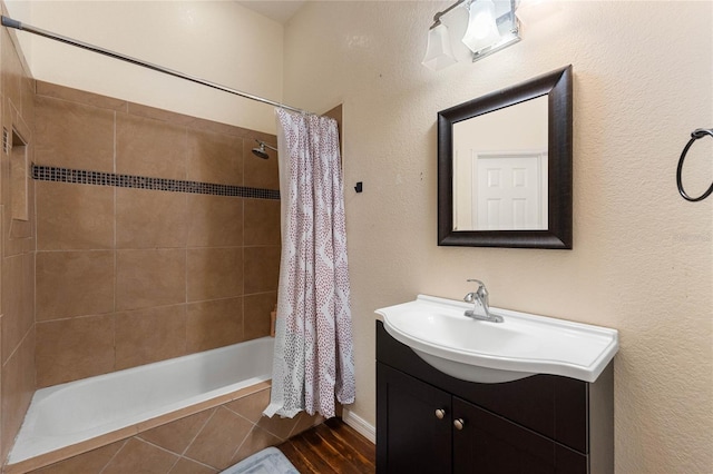 full bath with tiled shower / bath combo, a textured wall, wood finished floors, and vanity