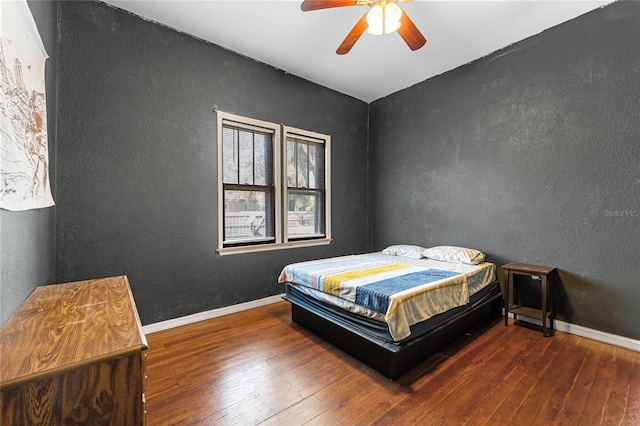 bedroom with baseboards, a textured wall, hardwood / wood-style floors, and ceiling fan