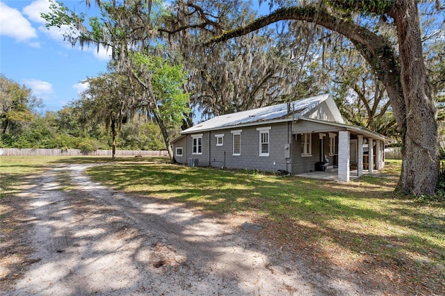 view of property exterior with concrete block siding, fence, metal roof, and a lawn