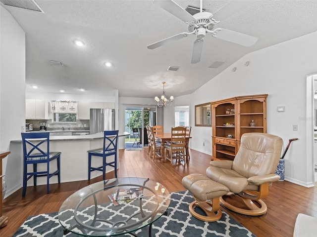 living area featuring lofted ceiling, dark wood-style flooring, visible vents, and ceiling fan with notable chandelier